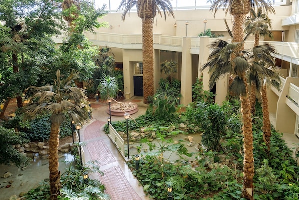 An indoor atrium with a central water feature, surrounded by palm trees and various plants.