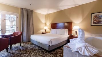 Une chambre d’hôtel comprenant un lit, deux lampes de chevet, une chaise, un bureau, une salle de bain avec baignoire et une porte donnant sur une vue de palmiers.