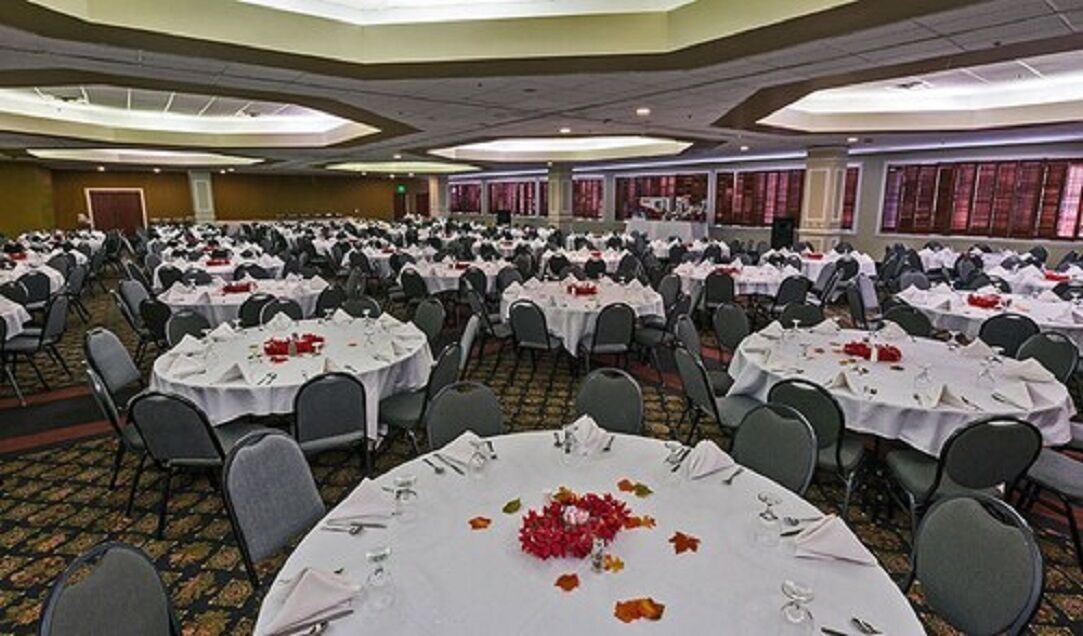 Une salle de banquet avec de nombreuses tables rondes disposées en rangées, prêtes pour le repas.