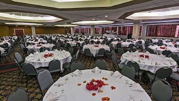 Une salle de banquet avec de nombreuses tables rondes disposées en rangées, prêtes pour le repas.