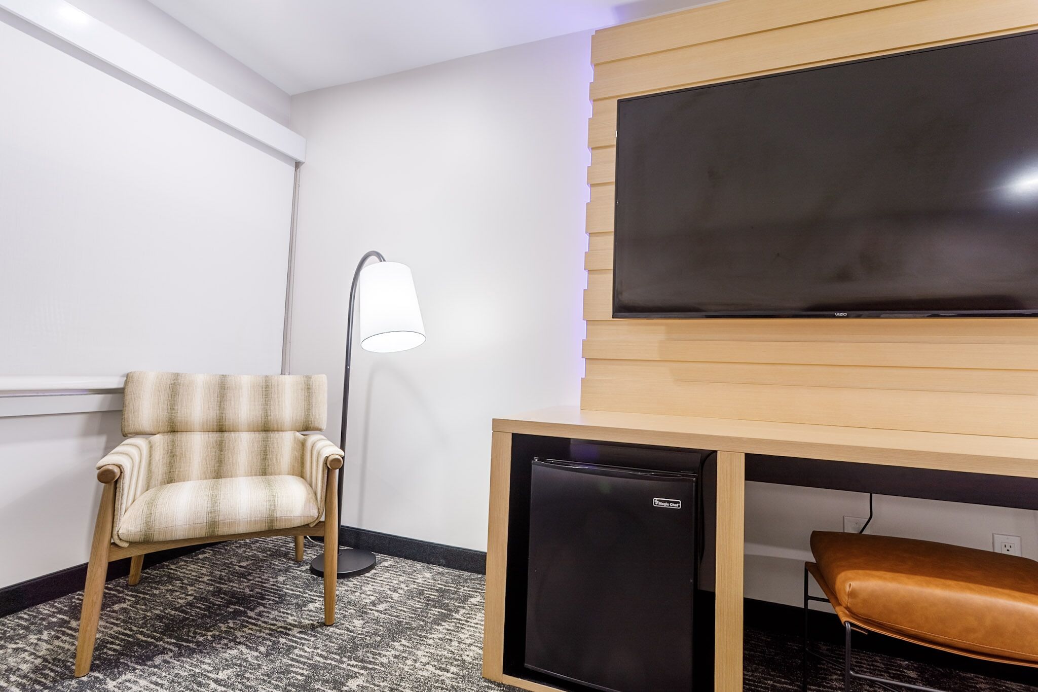 A room with a chair, a desk with a small black refrigerator, a lamp, and a large blackboard on the wall.
