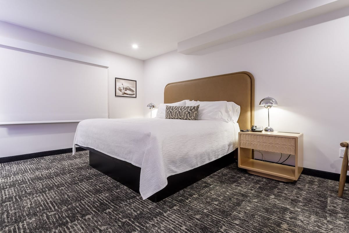 A hotel room with a large bed, a bedside table with a lamp, and a wall-mounted TV.