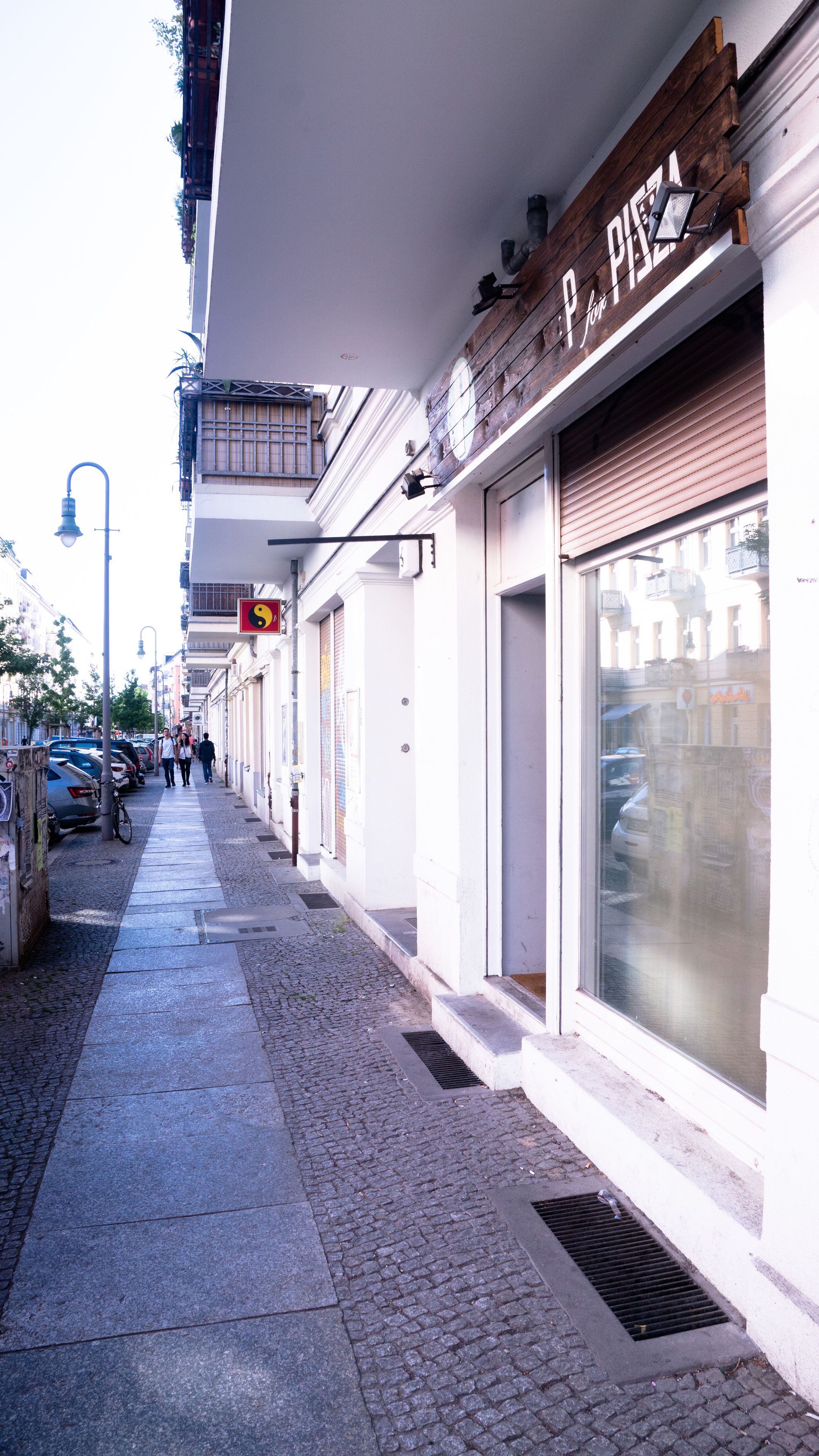 A narrow cobblestone street with storefronts, including a visible pizza shop.
