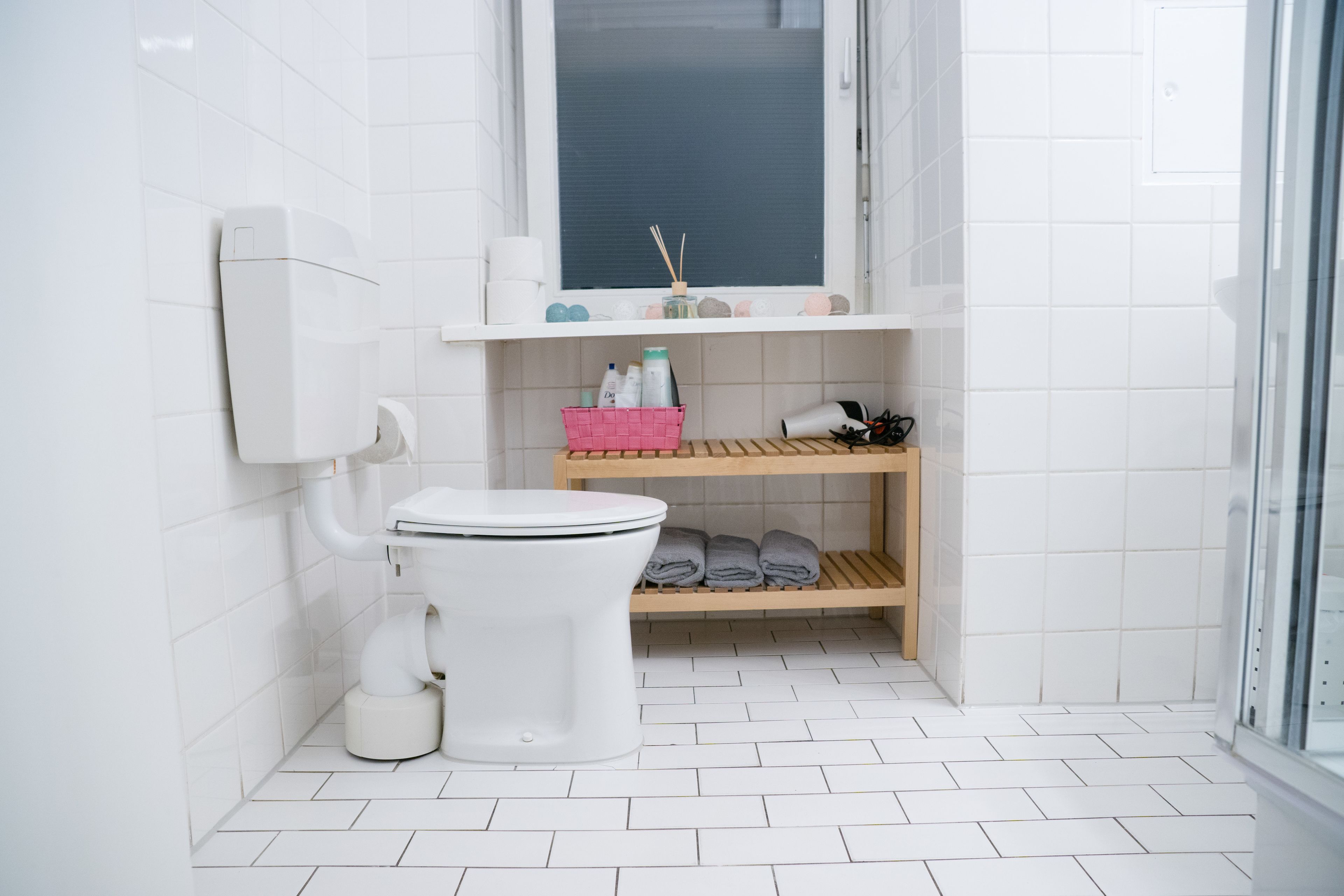 A modern bathroom with a toilet, a sink, a shelf with toiletries, and a window.