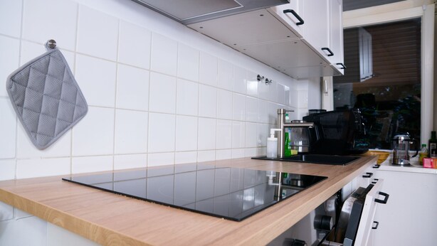 Una cocina moderna con encimera de madera, placa de inducción negra, paredes de azulejos blancos y campana extractora de acero inoxidable.