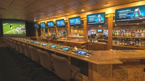 A bar area with multiple screens displaying sports events, a long counter with stools, and a variety of bottles and glasses on shelves. - Red Garter Hotel & Casino by Red Lion Hotels (West Wendover)