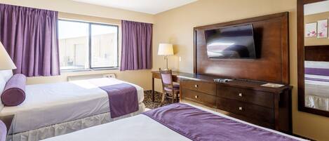 A hotel room with two beds, a TV, a desk, and a window with curtains.