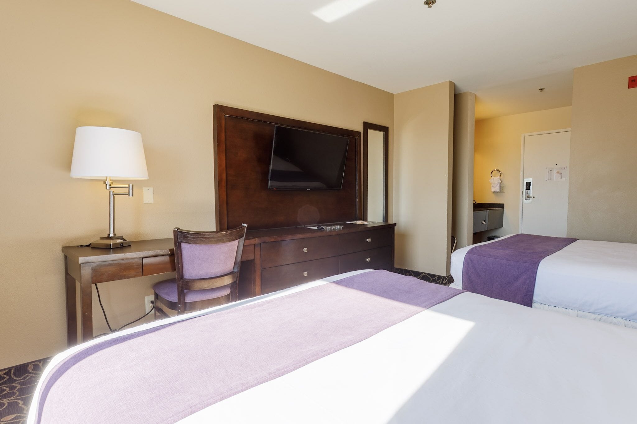 Una habitación de hotel con dos camas, un escritorio con lámpara, televisión y cómoda.
