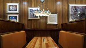 Un coin salon avec une table en bois et des sièges rembourrés, des tableaux encadrés au mur et un lustre suspendu.