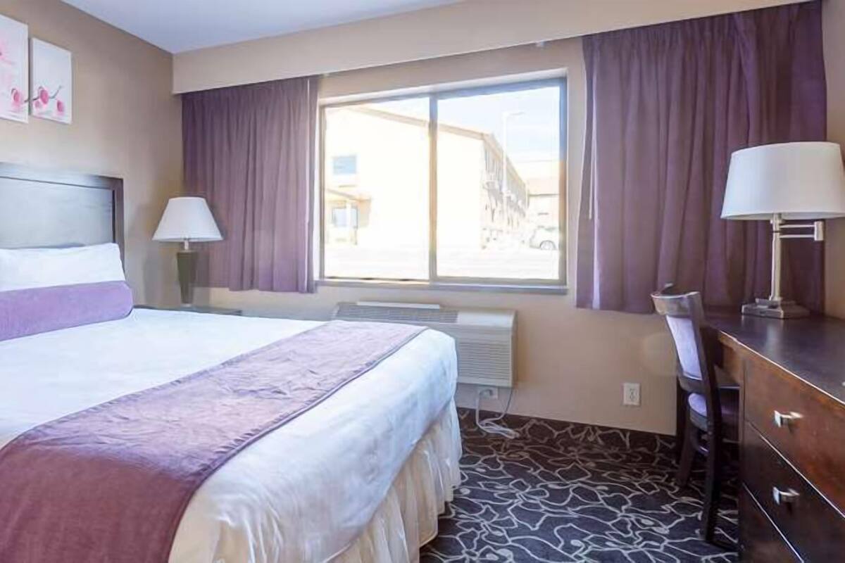 Una habitación de hotel con una cama grande, un aparador, una ventana con cortinas y una obra de arte en la pared.