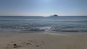 Uma praia com pegadas na areia, céu claro e uma ilha ao longe.