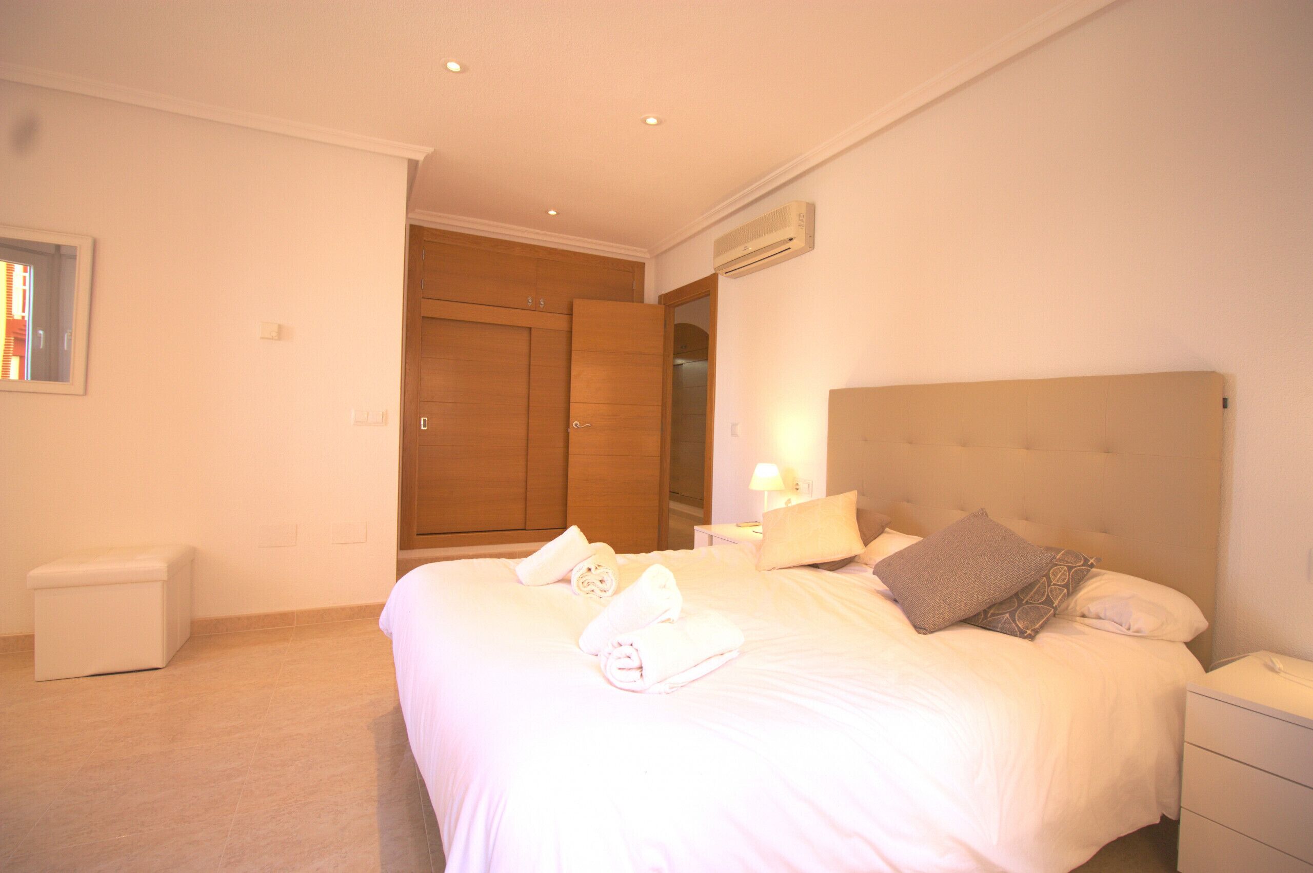 Ein Hotelzimmer mit einem großen Bett, einem Nachttisch mit Lampe, einem kleinen Nachttisch mit Telefon, einer weißen Mülltonne und einem Holzschrank.