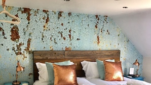 A bedroom with a sloped ceiling, a wooden headboard, a bed with white linens, two bedside lamps, and a blue dresser. - Meadowsweet Barn, Ashlin Farm Barns (Lincoln)