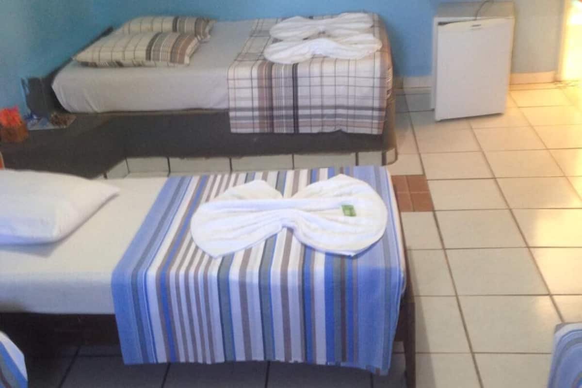 Una habitación de hotel pequeña con dos camas, un televisor, un refrigerador y un mantel a rayas.