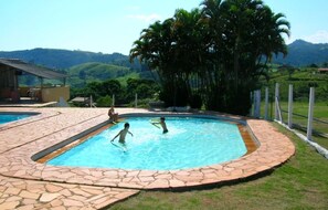 Una piscina con baldosas de piedra y vistas a colinas y palmeras.