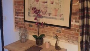 A room with a brick wall, a framed picture of ceramic items, a wooden table with a notebook, a potted plant, and a decorative metal sculpture. - Auberge de villechaume (Sennely)