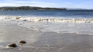 A beach with waves, a distant shoreline, and a clear sky. - Summertime Beach Cottage (Southport)