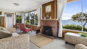 A cozy living room with a fireplace, wicker furniture, and a view of the ocean. - Summertime Beach Cottage (Southport)