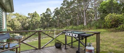 A wooden deck with a grill and a propane tank, surrounded by a grassy area and trees.