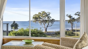 A room with a large window offering a view of the sea and trees. - Summertime Beach Cottage (Southport)