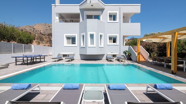 A modern building with a pool, lounge chairs, and a covered area with tables and chairs. - Villa Bella, 5 bedrooms with Private Pool, Hot Tub, Games Room near to beach (Lardos)