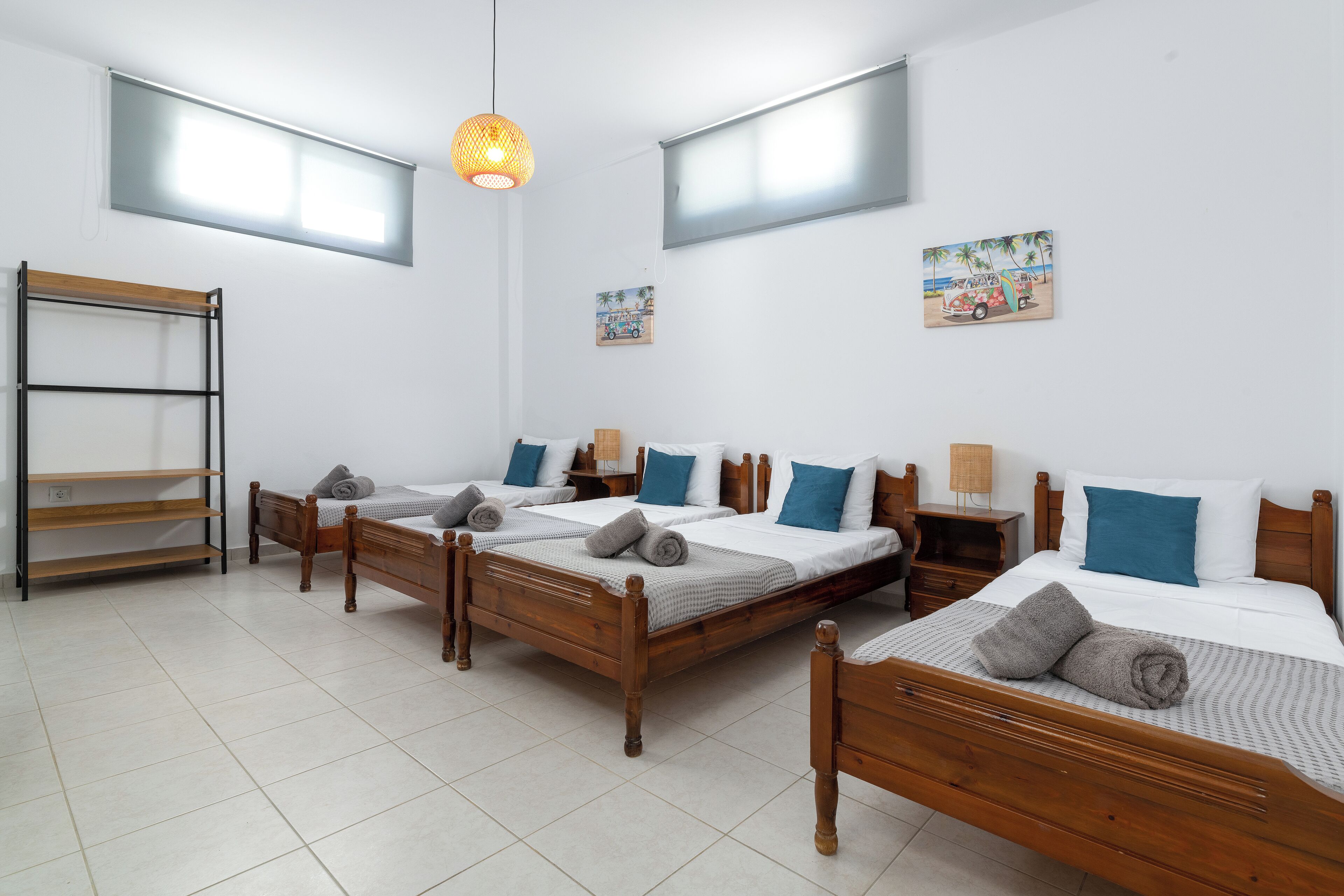 Habitación de hotel con tres camas de madera, una estantería de madera y una lámpara colgante.