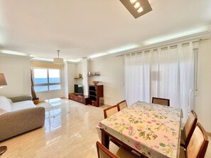 Una sala de estar con sofá, una mesa de comedor con sillas, un televisor y una ventana con cortinas.