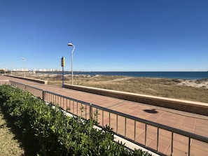 Ein Küstenweg mit Metallgeländer, blauem Himmel und Blick auf das Meer.