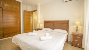 Een hotelkamer met een groot bed, een houten garderobe, twee nachtkastjes met lampen, en een airconditioning.