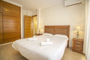 A hotel room with a large bed, wooden wardrobe, two bedside tables with lamps, and an air conditioning unit.