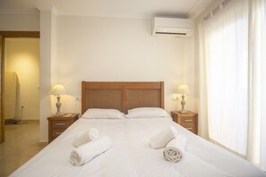 Hotellihuone, jossa on suuri sänky, kaksi yöpöytää valaisimineen, puinen sängynpääty ja ilmastointilaite.