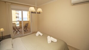Une chambre d’hôtel avec un lit, deux serviettes enroulées, une table de chevet, une lampe et une vue sur un balcon équipé de chaises et d’une table.
