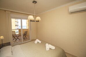 A hotel room with a bed, two rolled towels, a nightstand, a lamp, and a view of a balcony with chairs and a table.