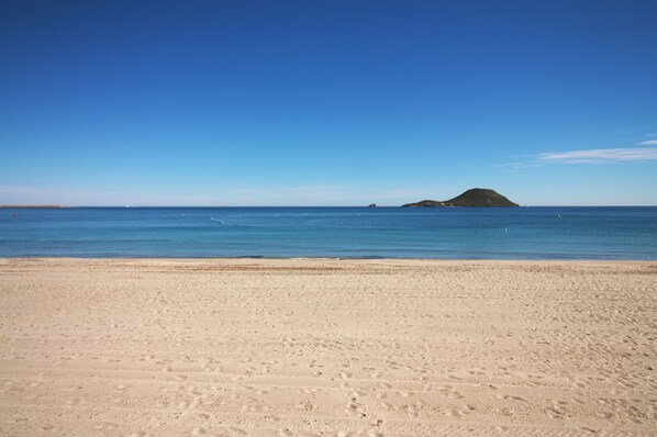 A beach with a clear sky, calm sea, and a distant island.
