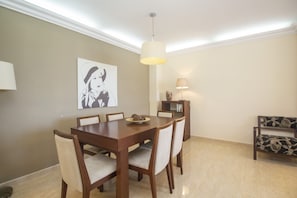 A dining area with a wooden table, six chairs, a chandelier, and a wall-mounted lamp.