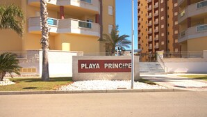 Une enseigne indiquant « Playa Princesa », offrant une vue dégagée sur la façade de l’immeuble, notamment sur les balcons et l’escalier menant à l’entrée.