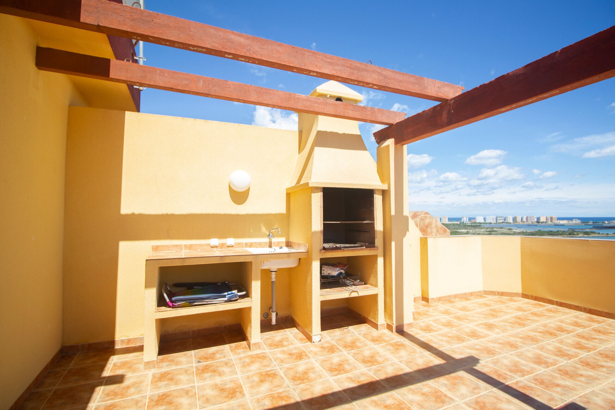 A balcony with a built-in grill, a sink, and a shelf with books.
