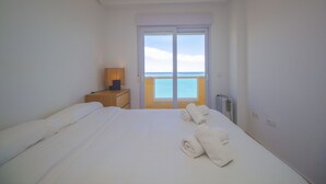 A hotel room with a bed, a nightstand, a lamp, and a view of the sea through a large window. - Superb penthouse perfectly located just steps from the beach... (La Manga del Mar Menor)