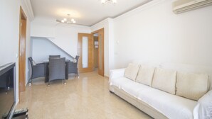 A modern living room with a sofa, a TV, a dining area with chairs, and a staircase leading to another room. - Superb penthouse perfectly located just steps from the beach... (La Manga del Mar Menor)