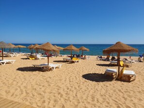 A beach with sun loungers and thatched umbrellas.