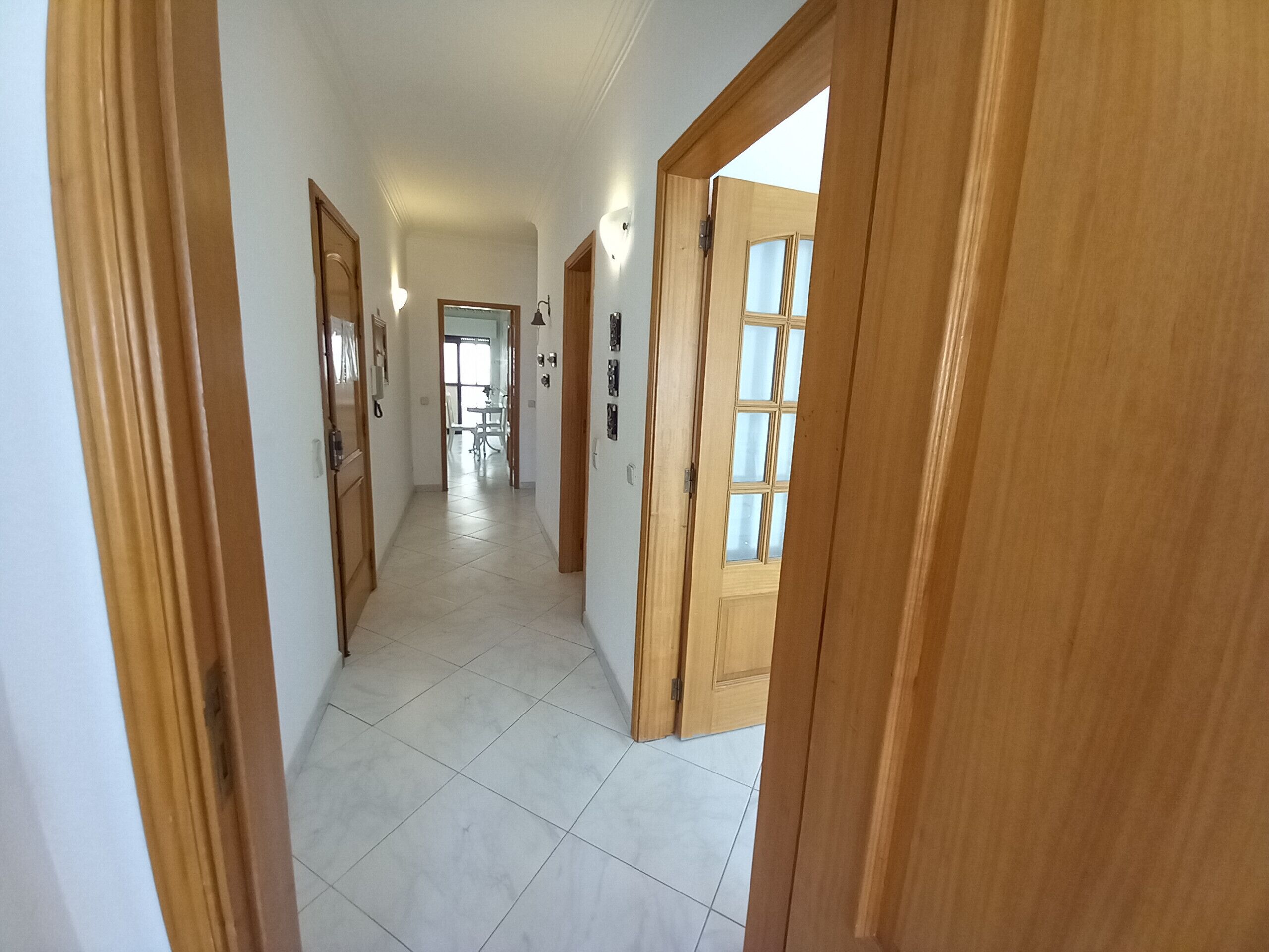 Un pasillo con puertas de madera y suelo de baldosas blancas que conduce a un comedor.