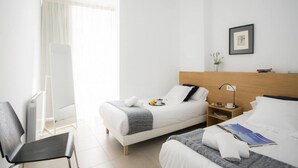 A hotel room with two beds, a chair, a bedside table with a lamp, a framed picture on the wall, and a radiator. - Singular Stays Mar44 I (Valencia ciudad)