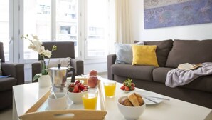 A modern living room with a sofa, a coffee table with breakfast items, and a large window. - Singular Stays Mar44 I (Valencia ciudad)