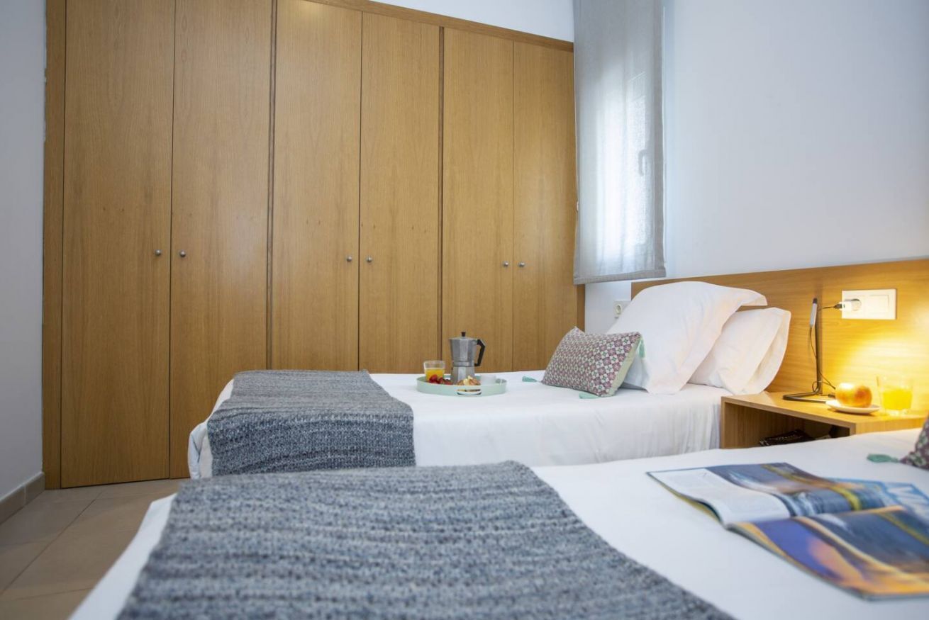 A hotel room with two beds, a wooden wardrobe, a bedside table with a lamp, and a breakfast tray on the beds.