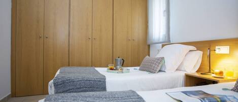 A hotel room with two beds, a wooden wardrobe, a bedside table with a lamp, and a breakfast tray on the beds.