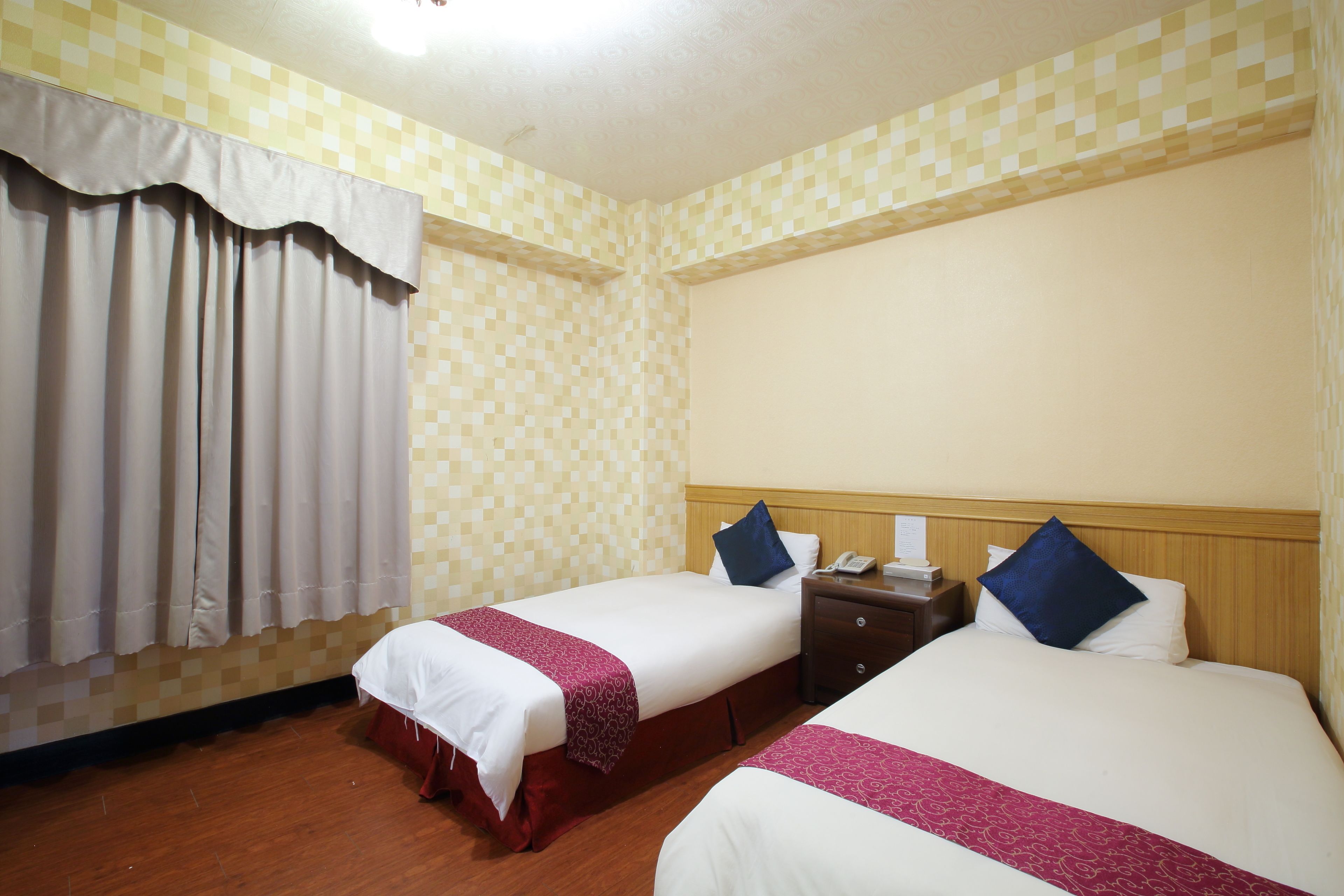 Quarto de hotel com duas camas, cabeceira de madeira, mesa de cabeceira e telefone.