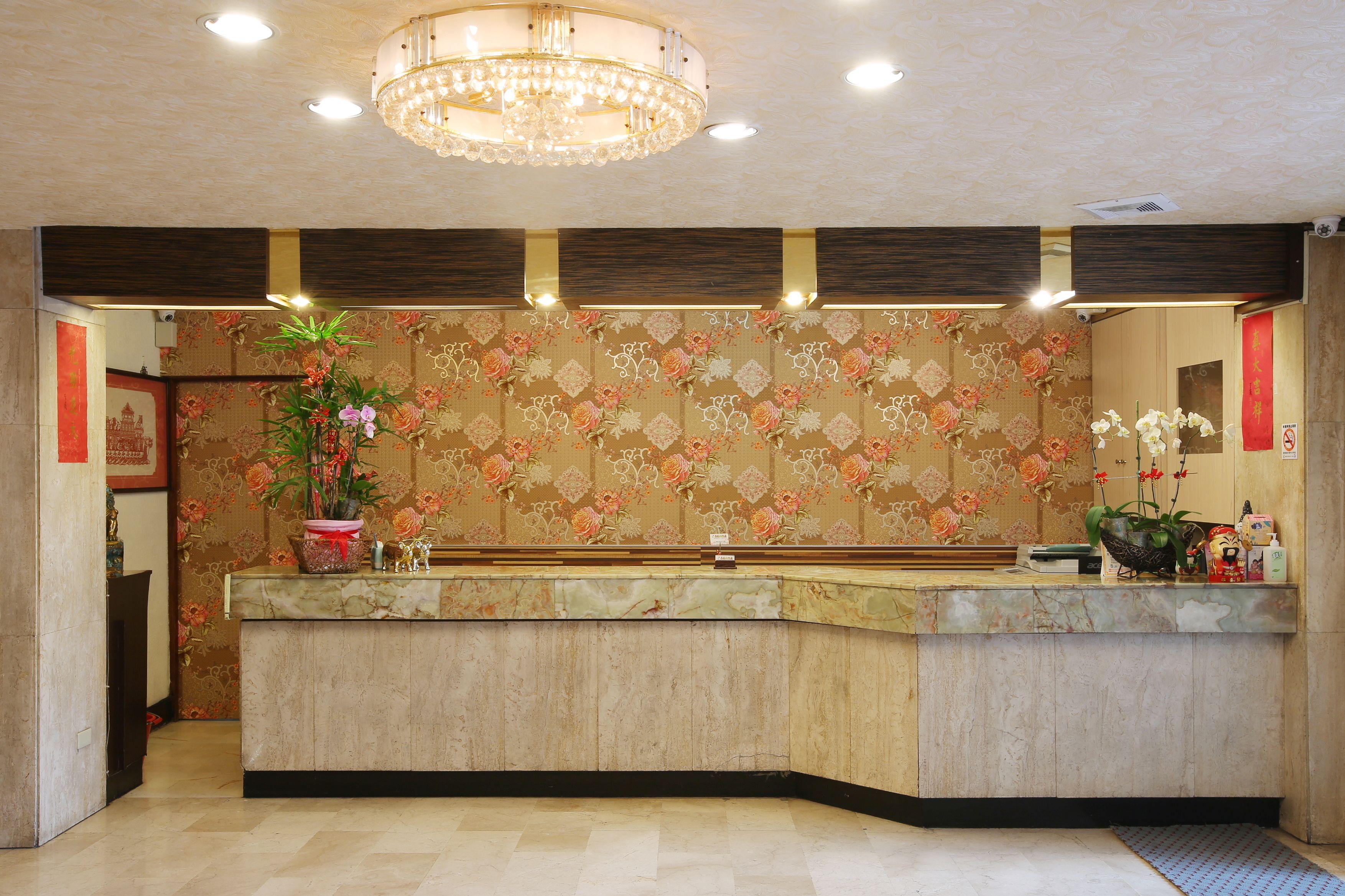 A reception area with a marble counter, floral wallpaper, a chandelier, and a red banner.