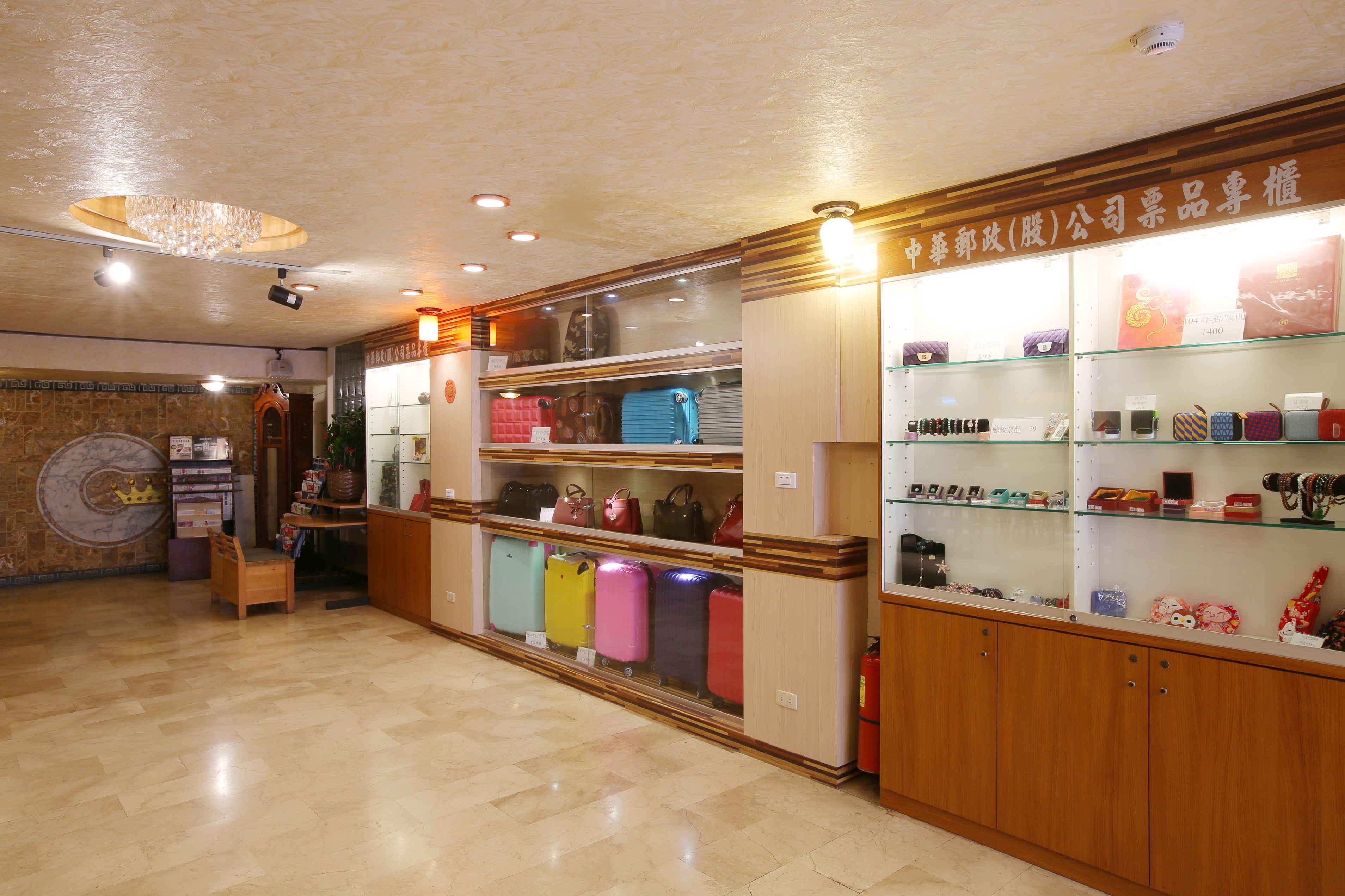 A hotel lobby with a wooden reception desk, a chandelier, and a display of colorful suitcases.