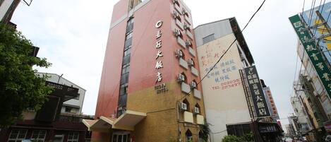 A hotel with a prominent red and beige facade, multiple balconies, and a visible entrance with a bicycle parked outside.