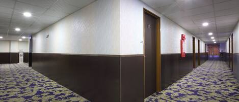 A hotel corridor with patterned carpet, a wooden door, and a red emergency exit sign.